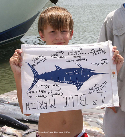THE PROOF IS IN THE FLAG: Holding an upside down marlin flag to signify the fish was released, young Connor is all smiles back at the dock. Photo by Conor Harrison, LSON. connorkelly