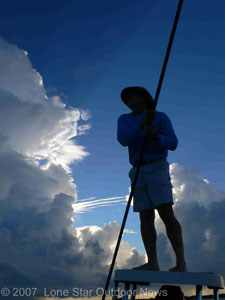 Capt. Paul Brown poles his skiff in search of Red Drum tails near California Hole. A morning thunderstorm looms in the background. Photo by David J. Sams